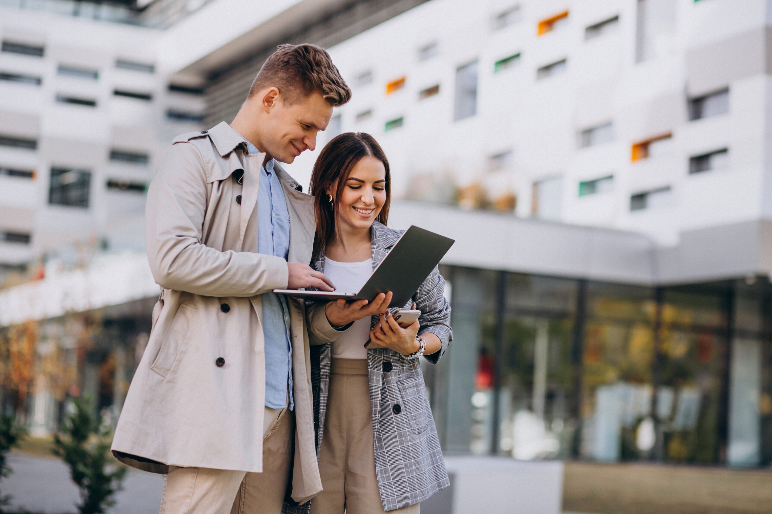 Young couple standing together outside and using computer